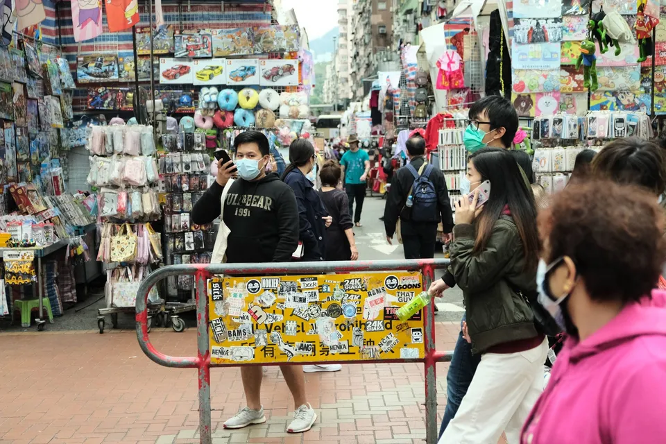 a crowd of people walking down a street next to a store filled with merchandise and a man wearing a face mask