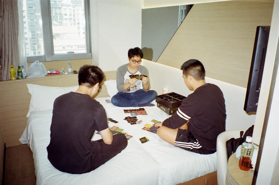 Three male adults sitting on the bed playing board game 7 Wonders