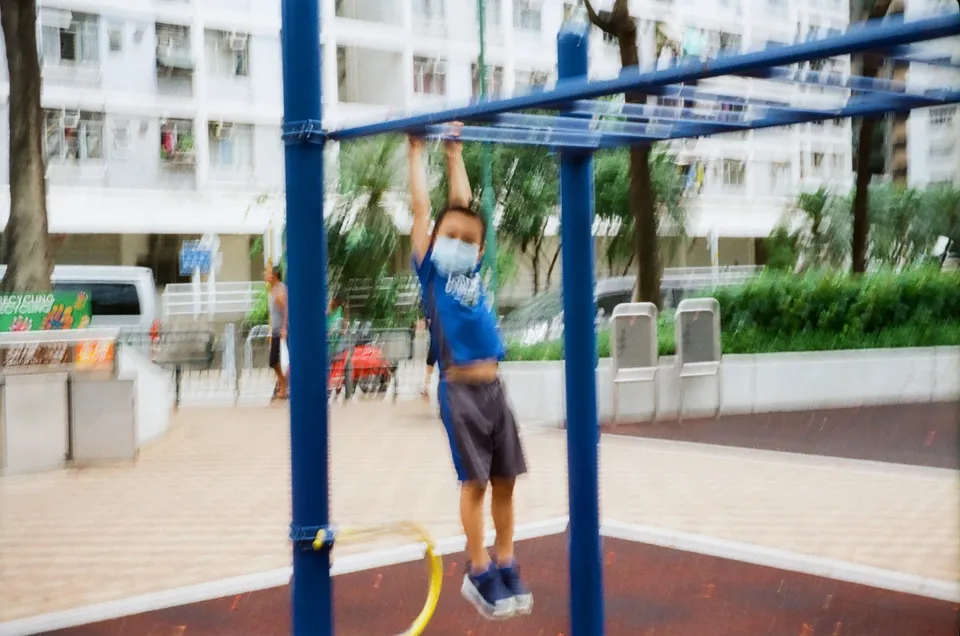 a child is playing on a playground with a yellow tube and a blue pole in front of him and a building in the background